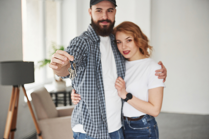 Young couple smiling at home with man holding house keys, related to schizophrenic man prank hospital visit concept