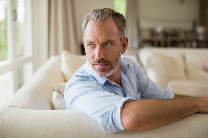 Middle-aged man looking thoughtful while sitting on a couch, reflecting on things people would never admit in real life.