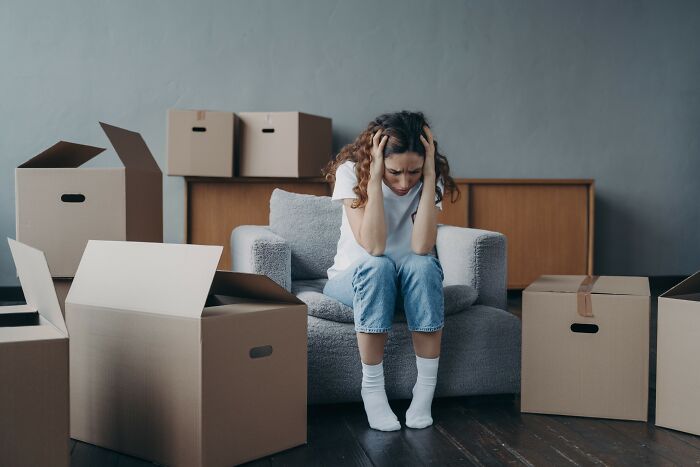 Frustrated woman sitting on a couch surrounded by cardboard boxes, feeling out of touch and overwhelmed.