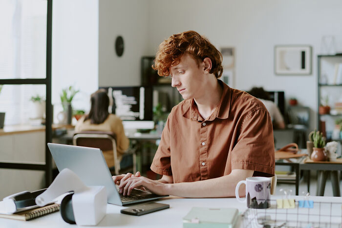 Young employee working on laptop in modern office, illustrating insider tricks that make jobs easier for employees.