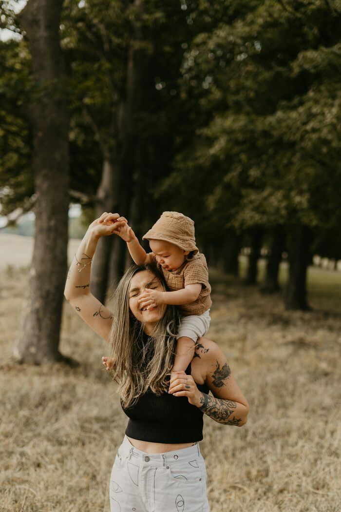 Woman with tattoos smiling outdoors while carrying a toddler on her shoulders, reflecting on school bullies stories.
