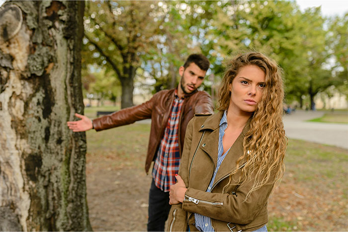 Young tall man pleading with an old friend in a park while she looks upset and crosses her arms.