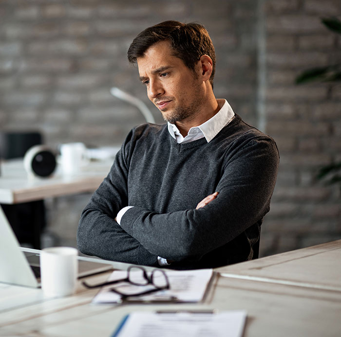 Man in a gray sweater sitting at a desk looking thoughtful, reflecting on lies that changed someone's life.
