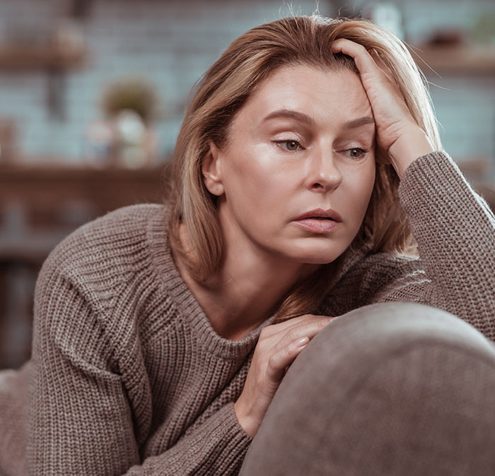 Woman in a brown sweater looking thoughtful and worried indoors, reflecting on lies that changed someone else's life.