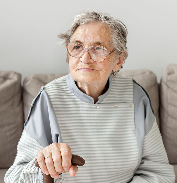 Elderly woman with glasses sitting on a sofa, holding a cane, reflecting on lies that changed life outcomes.
