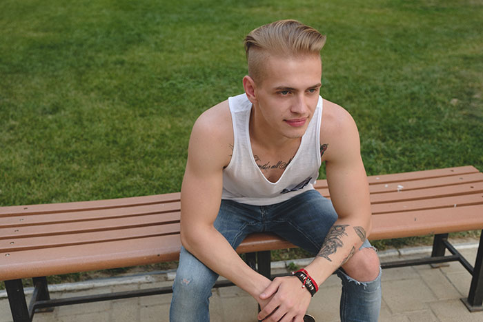 Young man with tattoos sitting on a bench outdoors, reflecting on life changes caused by lies.