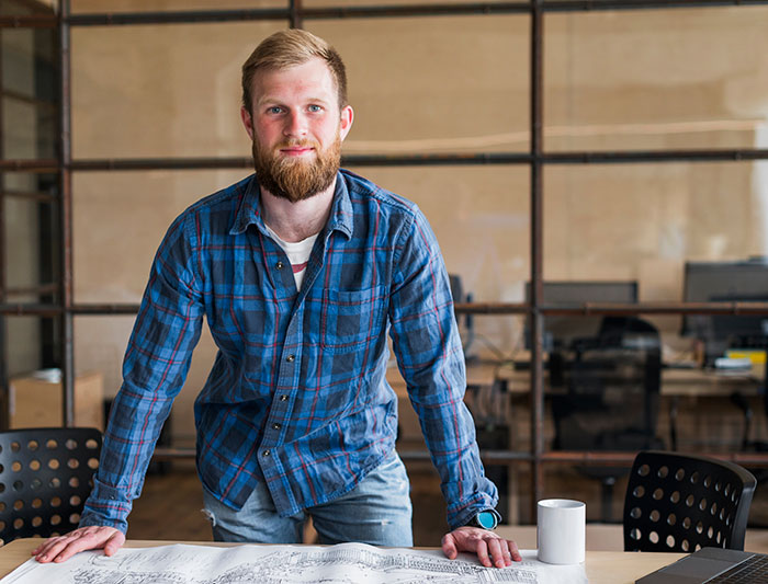 Young man in a blue plaid shirt standing by a desk, representing lies that changed someone else's life for better or worse.
