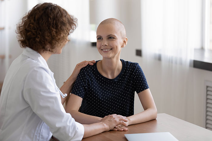 Young woman with cancer smiling at doctor who is comforting her during a supportive medical consultation about life changes.