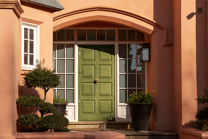 Green front door entrance with plants and sunlight on peach-colored house exterior, symbolizing life changes through lies.