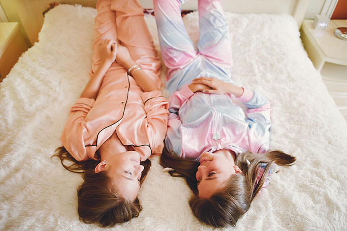 Two girls in colorful pajamas lying on a bed facing each other, reflecting on lies that changed someone else’s life.