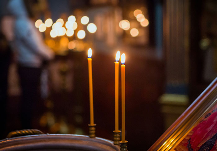 Three lit candles in a dimly lit setting with blurred lights and a person in the background, related to worst tourists seen.