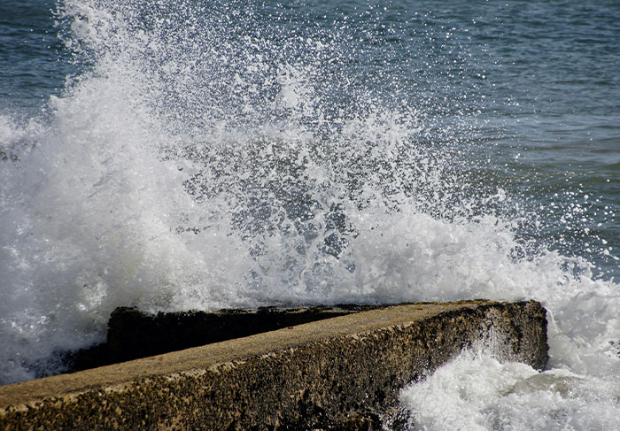 Ocean waves crashing against a concrete pier with tourists facing risky situations near rough water on tour guides' worst experiences.