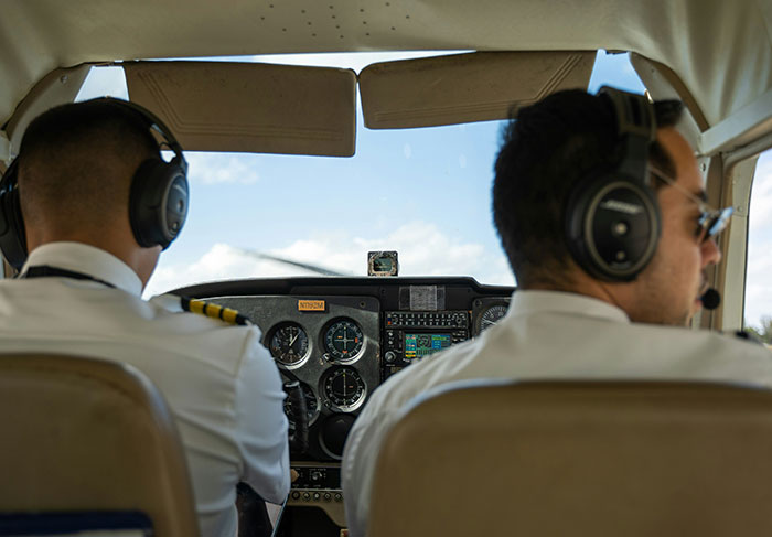 Two pilots wearing headsets navigating a small aircraft cockpit with clear skies visible outside.