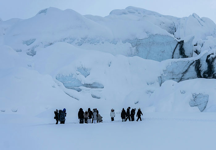Group of tourists dressed in winter clothing exploring a snowy glacier landscape with ice formations behind them.