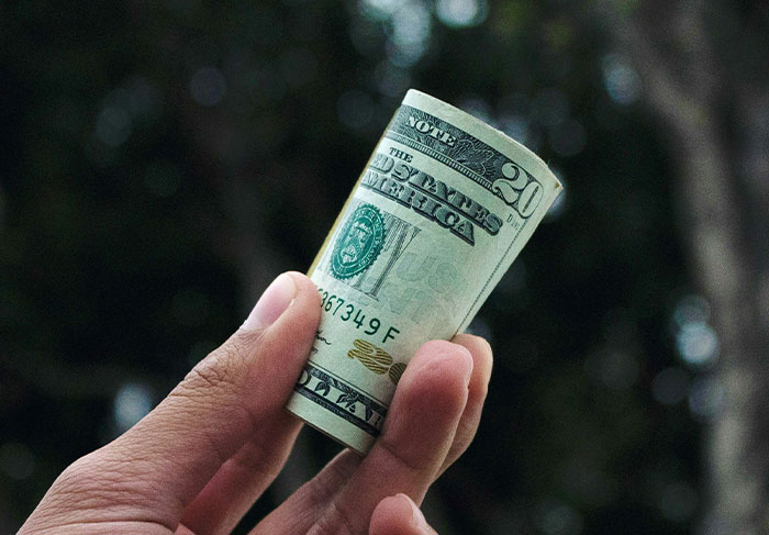 Hand holding a rolled twenty dollar bill representing tourists risking for worst tourist stories by tour guides.