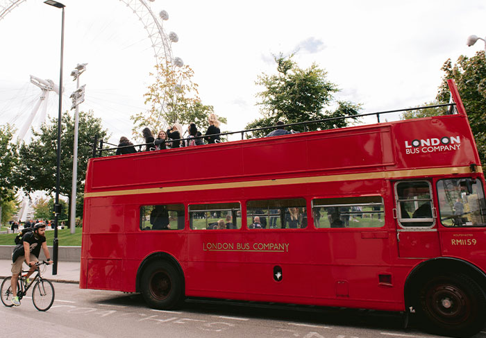 Red double-decker bus with tourists on top near London Eye, showcasing worst tourists seen by tour guides in busy city setting.