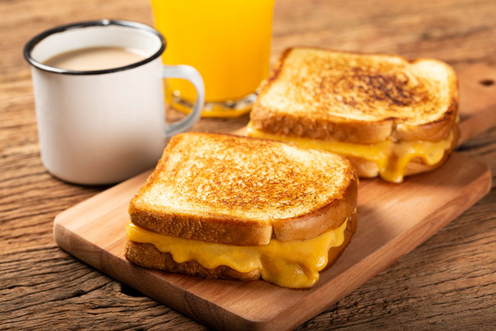 Grilled cheese sandwiches with melted cheddar served on a wooden board alongside coffee and orange juice, employee quits concept.