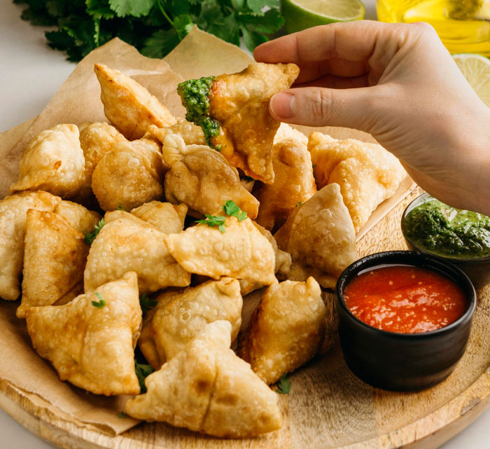 Hand picking crispy fried samosa with green chutney, symbolizing an ambush or surprising act in a workplace scenario.