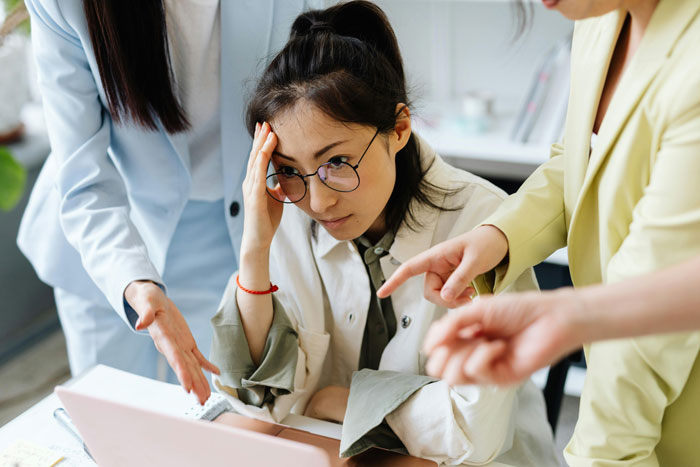 Stressed employee facing disciplinary hearing while her toxic bosses point fingers in a tense office setting.