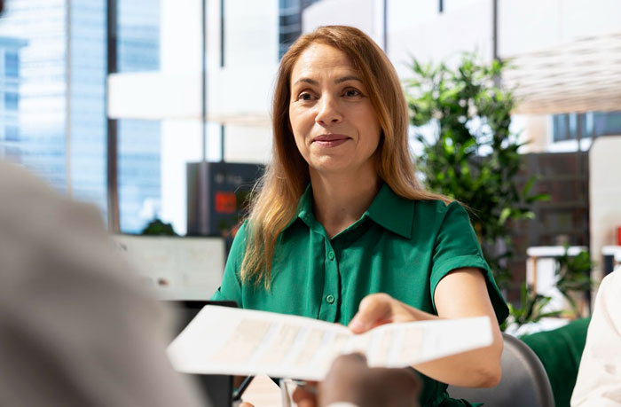 Employee in green shirt handing document during a tense meeting, highlighting workplace ambush and toxic bosses scenario.