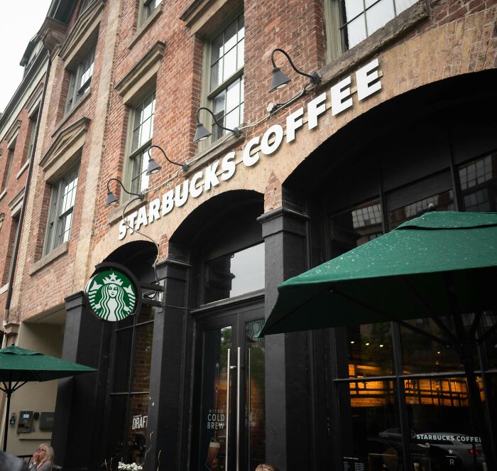 Starbucks store exterior with brick walls and green umbrellas, related to Charlie Kirk's favorite Starbucks drink story.