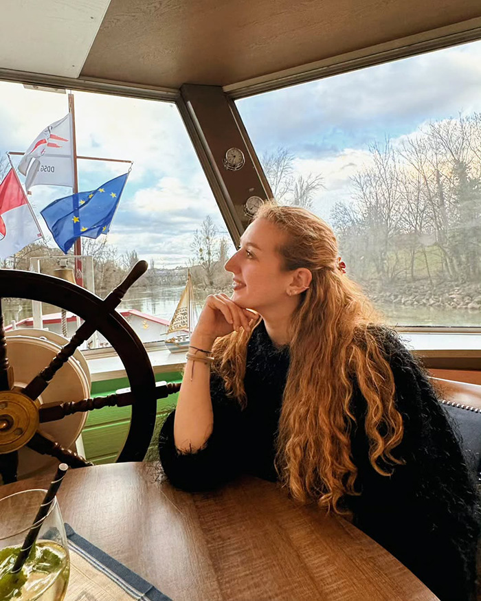Young woman with long hair sitting by a window inside a boat, unrelated to trapeze artist losing life during circus stunt.