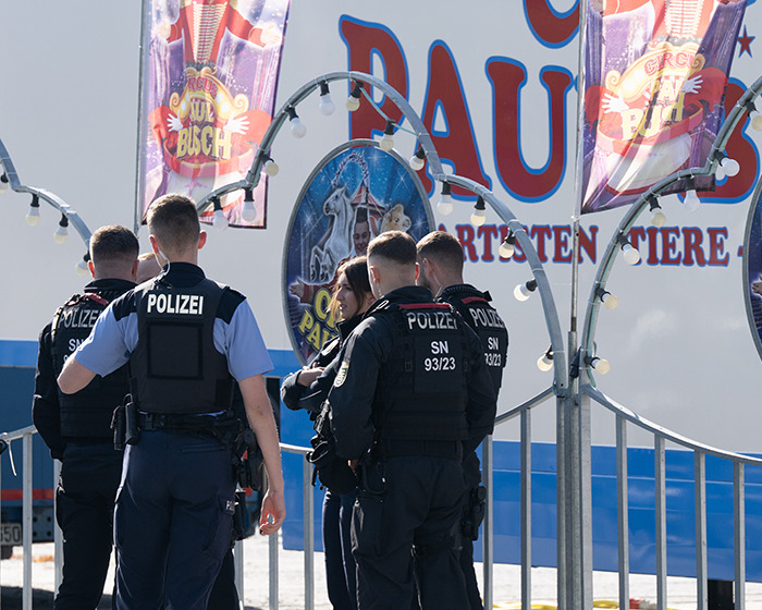 Police officers standing outside circus venue after trapeze artist accident during stunt in front of stunned families.