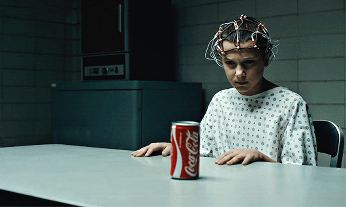 Young person in a hospital gown with brain monitoring device, staring intensely at a can of Coca-Cola, illustrating bizarre real life.