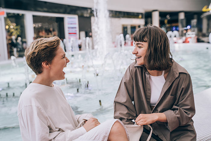 Two women engaging in a lively conversation near a fountain, capturing a moment without shallow or judgmental behavior.