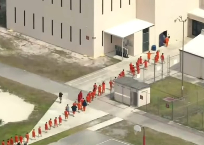 Detainees in orange uniforms walking in line inside a secured facility missing from ICE records after Alligator Alcatraz transfer