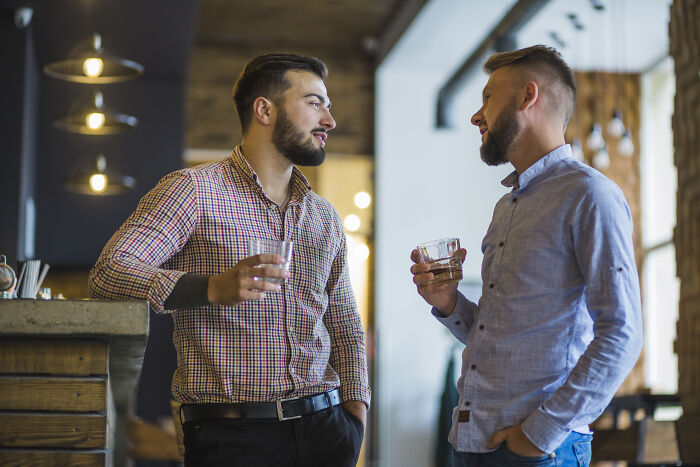 Two men having a casual conversation while drinking water in a modern cafe, illustrating advanced stupid moments.