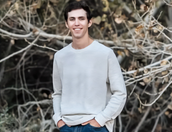 Tyler Robinson in a casual white sweater standing outdoors with hands in pockets, linked to Charlie Kirk suspect court appearance.