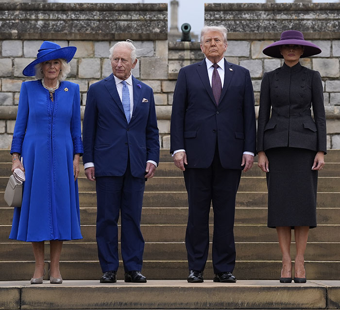 First Lady wearing a dark outfit and hat in the UK, standing beside leaders during a formal event on stone steps. First Lady wearing a dark outfit and hat in the UK, standing beside leaders during a formal event on stone steps.
