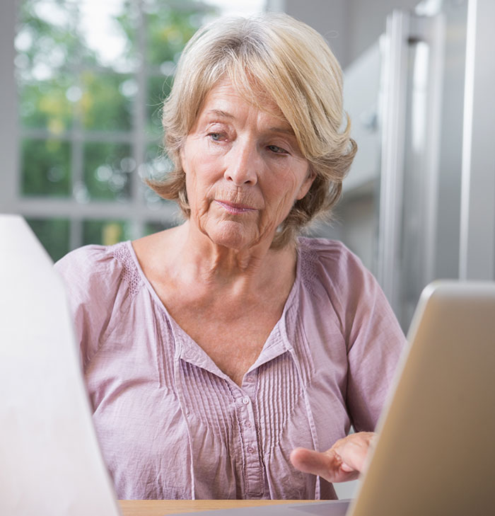Older woman looking concerned using laptop, depicting mother-in-law hijacking pregnancy on social media profile.