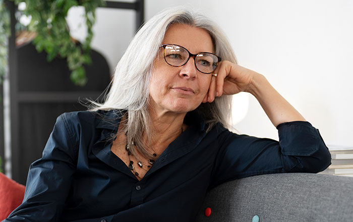 Middle-aged woman with glasses resting on a couch, reflecting on a story about hijacking pregnancy on social media.