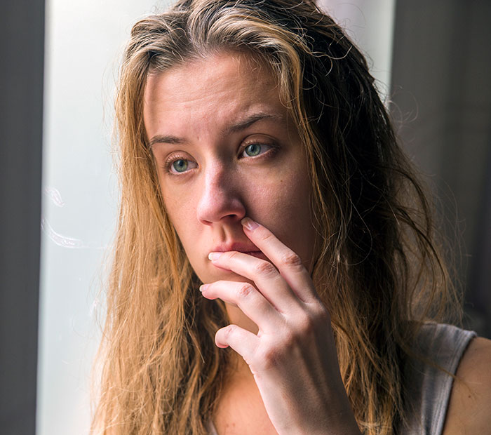Woman with tousled hair looking out a window, appearing thoughtful and concerned about pregnancy and family issues.