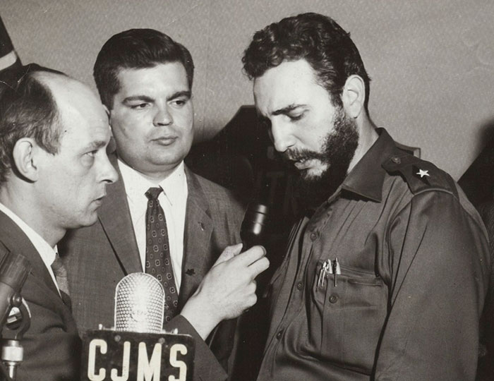 Black and white photo of a historical event showing a man in military uniform giving a serious interview to reporters.