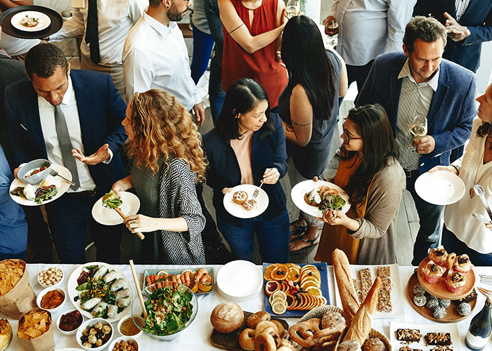 Group of people networking and enjoying food at an event, discussing industry secrets and business insights informally.