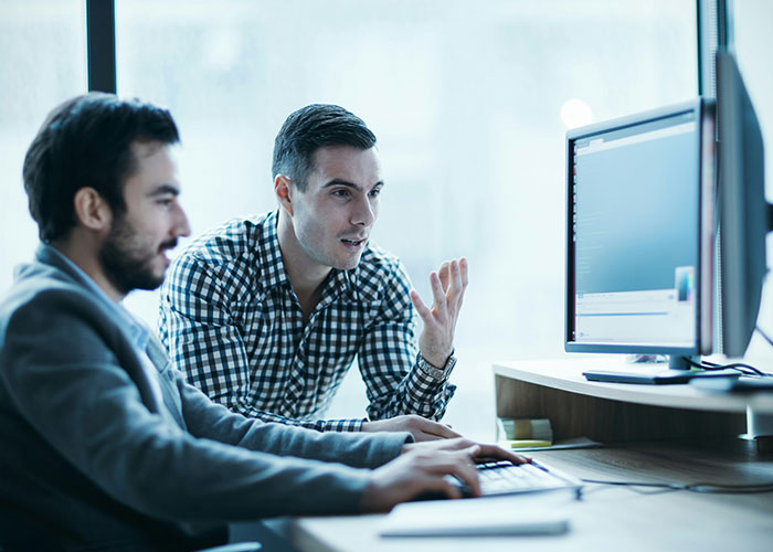 Two men discussing unexpected industry secrets while working together at a computer in an office environment