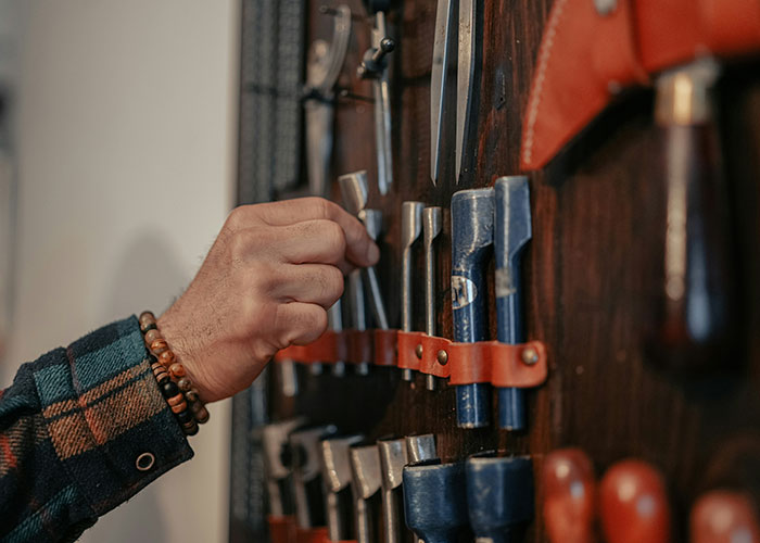 A person selecting a chisel from a wall-mounted tool organizer showcasing industry secrets in craftsmanship.