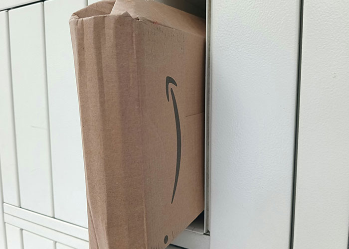 Close-up of a damaged cardboard delivery box partially inserted in a locked storage compartment, highlighting industry secrets.