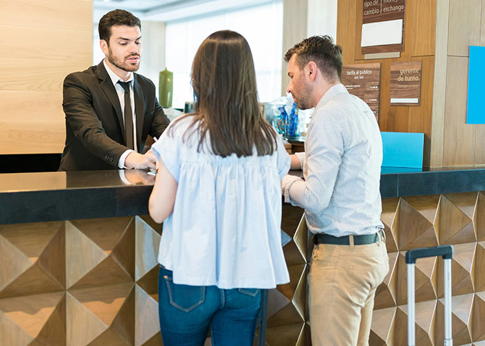 Hotel receptionist in a suit assisting guests at the counter, revealing unexpected industry secrets in hospitality services.