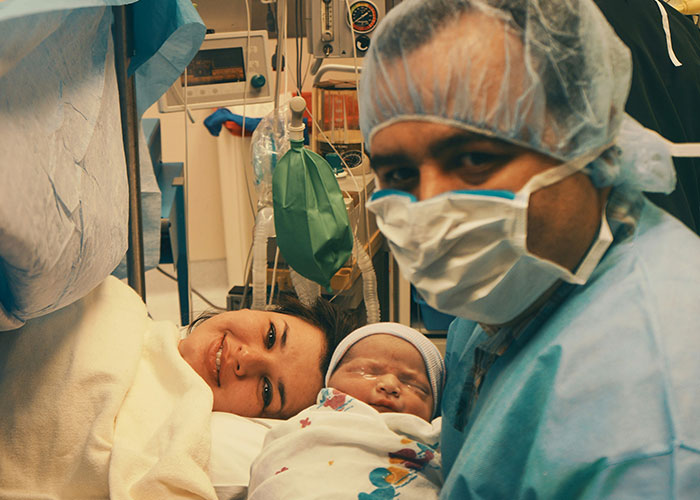 Newborn baby in hospital with mother and masked healthcare professional sharing industry secrets in medical care.