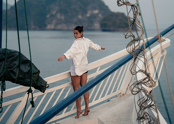 Woman in white shirt standing on a boat railing by the water, enjoying a peaceful moment with industry secrets vibe.