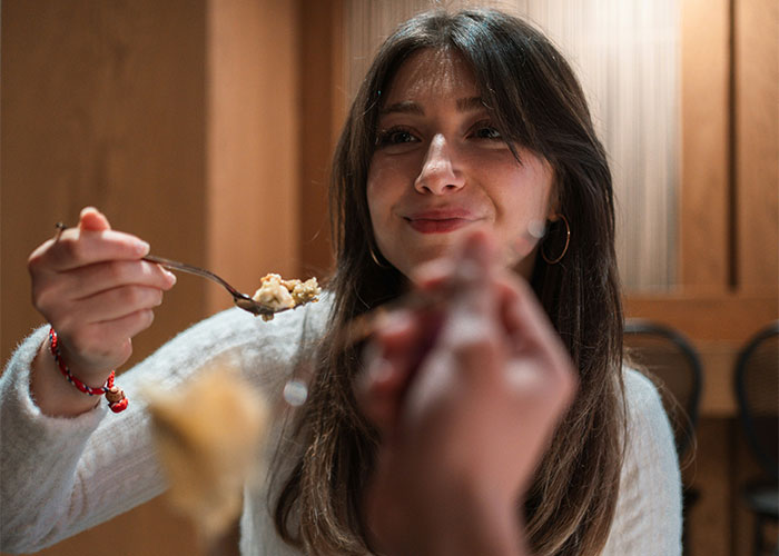 Young woman smiling and sharing food, enjoying a casual moment with industry secrets in the background ambiance.