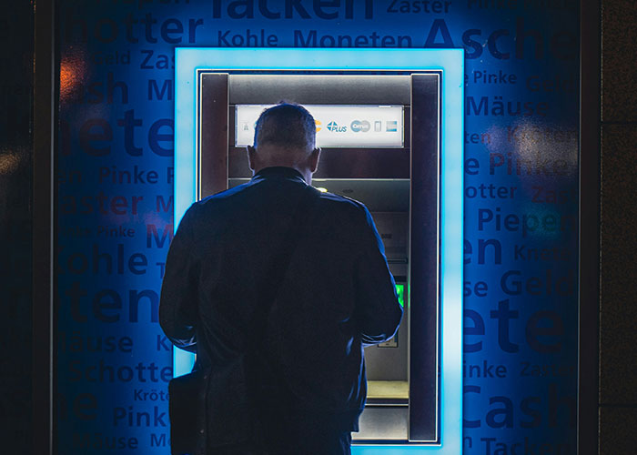 Man using ATM machine at night illuminated by blue light, illustrating industry secrets outsiders don’t know about.