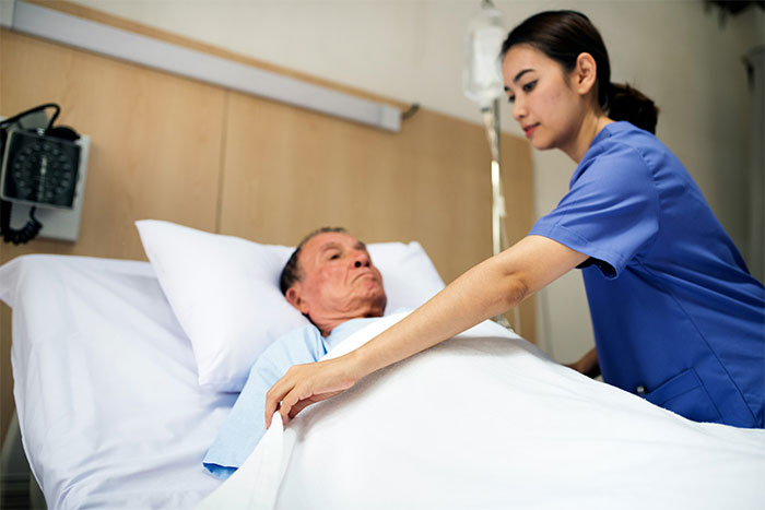 Nurse adjusting blanket for elderly patient in hospital room, illustrating bizarre and paranormal experiences concept.