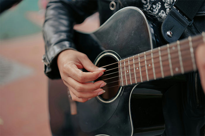 Person wearing a leather jacket playing a black acoustic guitar, capturing a moment of bizarre and paranormal experiences.