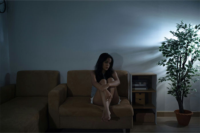 Woman sitting alone on couch in dark room with mysterious lighting, illustrating bizarre and paranormal experiences concept