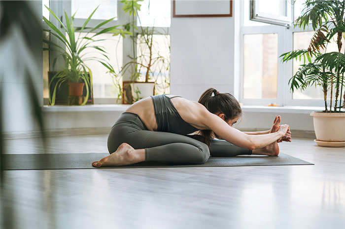 Woman practicing yoga indoors on a mat surrounded by plants, illustrating relaxation amid bizarre paranormal experiences.